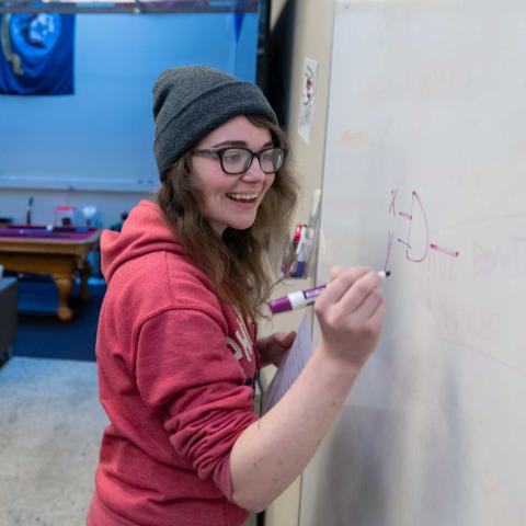 person standing at a white board writing and smiling