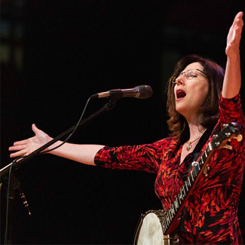 a woman singing onstage with her arms held up.