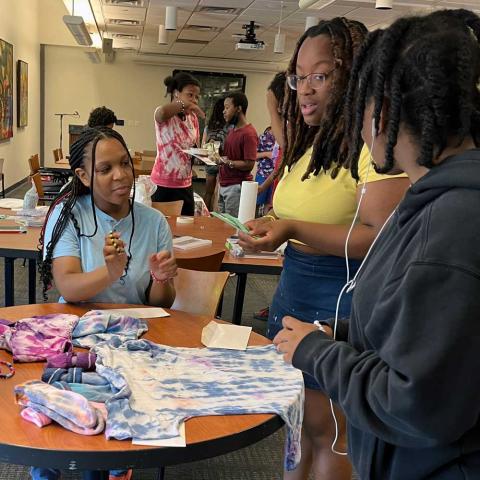 Three people seated around a table working on a tie-die t-shirt