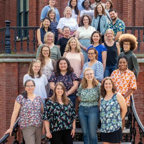 A group of people gathered on the steps of a brick building smiling for the camera