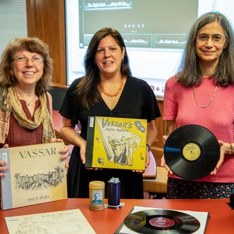 Three women, one holding a record, the other two holding old record album books 