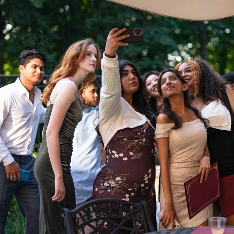 A large group of people huddled together outside with one person holding up their phone for a group selfie.