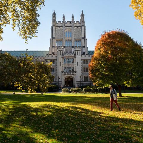 Pictured: Vassar Library. An old light colored brick building with a castle style towner in the center. There are green trees and grass in the foreground.