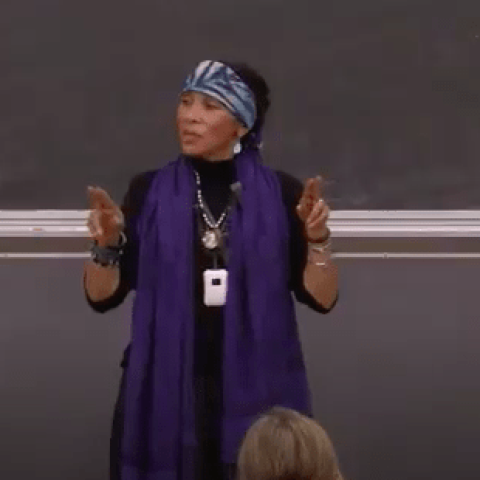 Person standing in front of a chalk board addressing an audience.