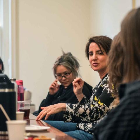 Five seated people at a table listening to one person, also at the table, speaking.