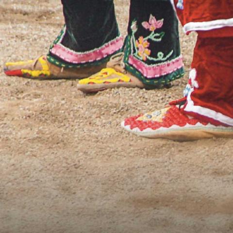 Three feet dressed in traditionally decorated Native American moccasins.