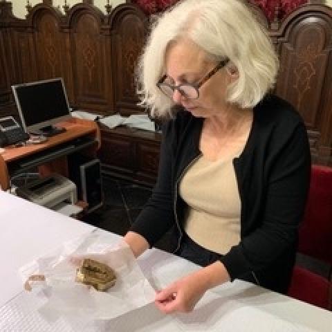 Julie Harris sitting at a desk, looking at a gold object wrapped in tissue paper.