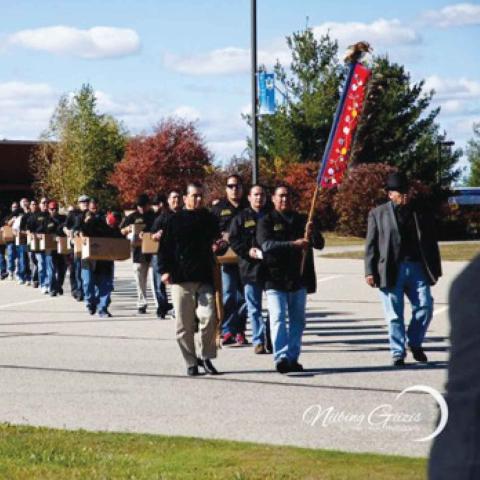 people in a parking lot walking behind a leader holding a flag.