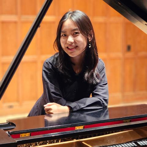 Looking through a piano with the top raised, a person leaning forward and smiling.