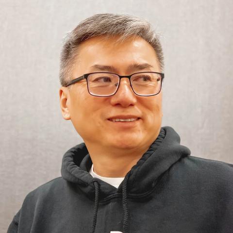 A person with a dark grey hoodie, glasses, and greying hair.