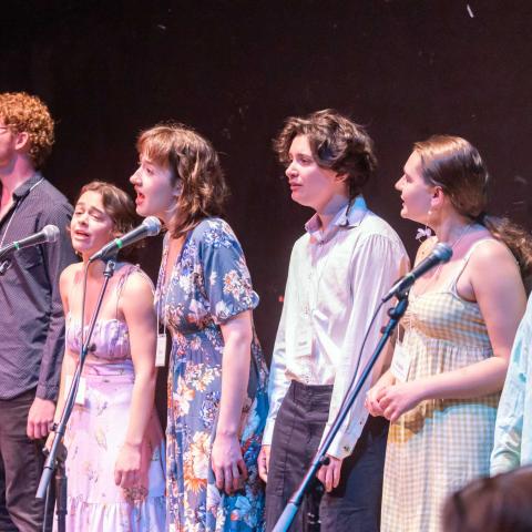 A group of people on staging standing behind microphones singing.