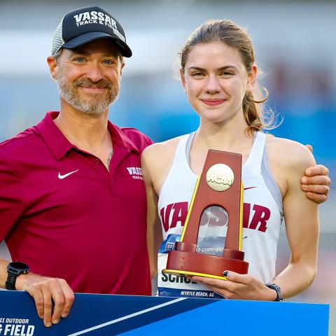 Couch and athlete standing together facing the camera, smiling proudly.