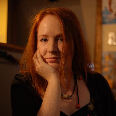 Person sitting in a dark room with long red hair resting their chin on their palm.