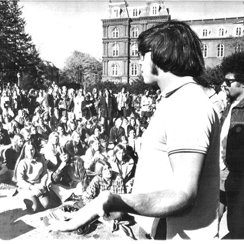 An old black and white image of a large gathering of people standing outside with Main building in the background.