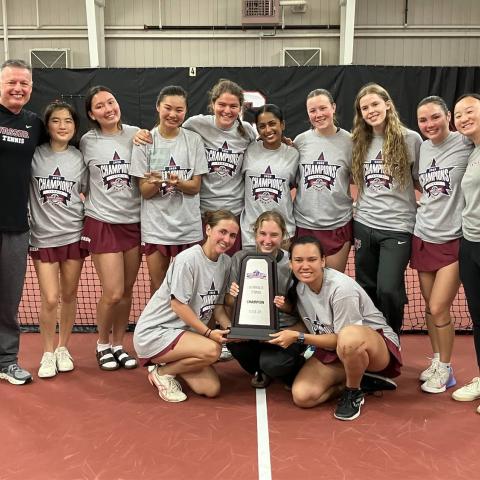 Team photo on a tennis court with a trophy.