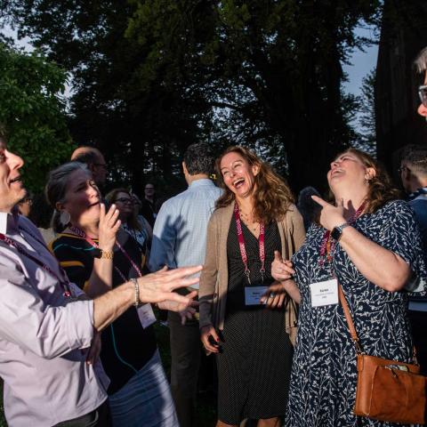 A group of people standing, laughing and talking outside at night.