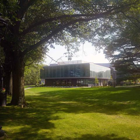 Exterior photo of a building surrounded by large trees and a grass lawn.