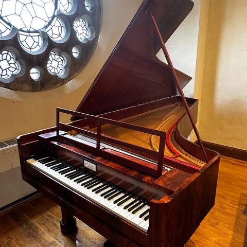 the Schubert era piano with the lid open, in front of a stained glass circular window.