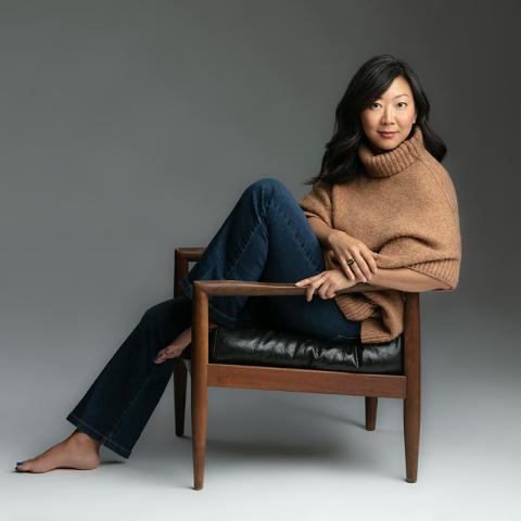 Portrait of a person sitting on a chair with on leg up and one down with no shoes..