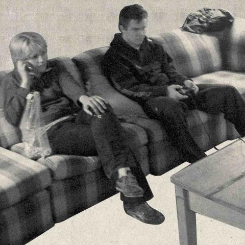 A monochrome halftone photo shows two people sitting on a couch watching television. The image is a selection from the poster for the film "Secret Mall Apartment".