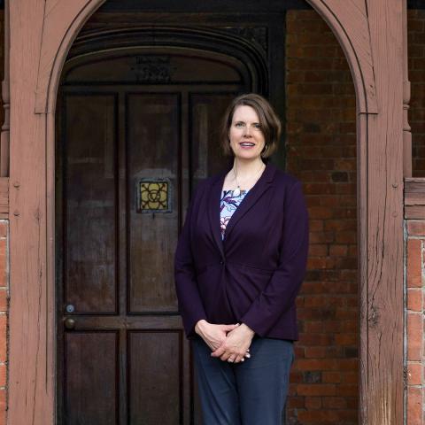 Callista Isabelle in a purple blazer stands in front of a wooden doorway at Pratt House.