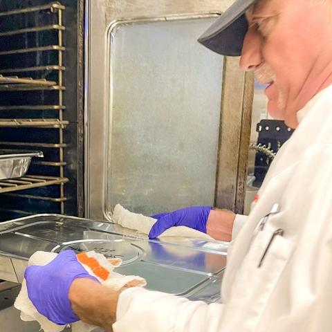 A person in cooking garb sliding glass cookware into an oven.