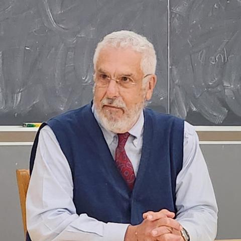 Person seated at a classroom table in front of a chalkboard.