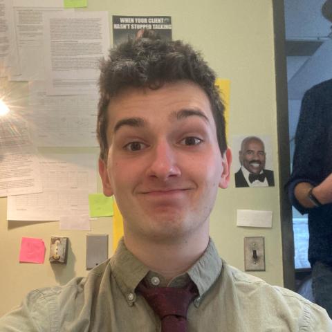 Pictured: Cole Smith. Person smiling at he camera in an office while wearing a tie.