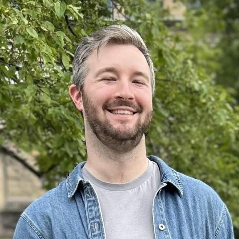 Photo portrait of a person standing in front of green foliage.
