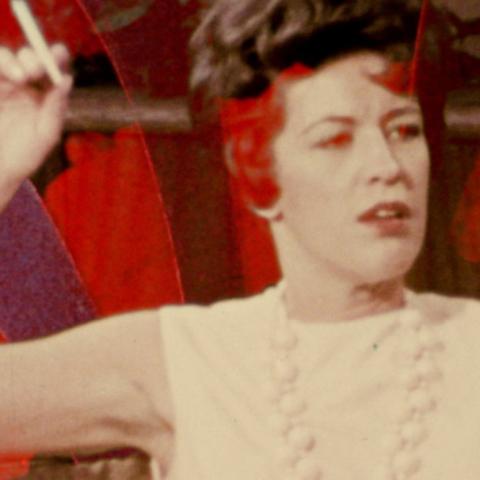 Film still of a close up of a seated person holding a cigarette while looking on.