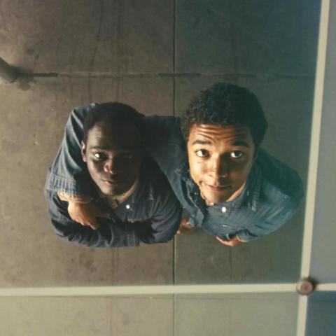 Two smiling people, arm in arm, looking up at a camera above them.