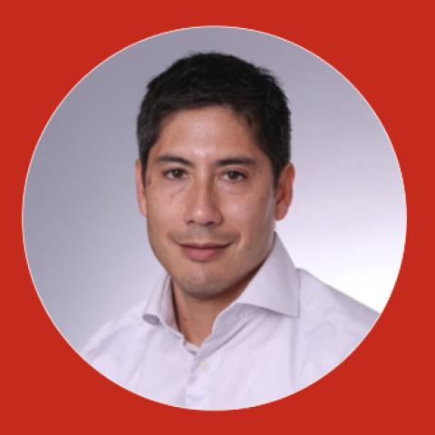 Headshot of a man with short dark hair, wearing a white button-down shirt, softly smiling, on a light gray background within a circular crop on a red field.