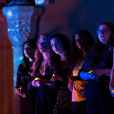 Detail of performers on a dramatically lit stage, holding candles.