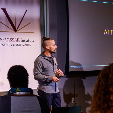 Person standing in front of a seated audience while addressing them.