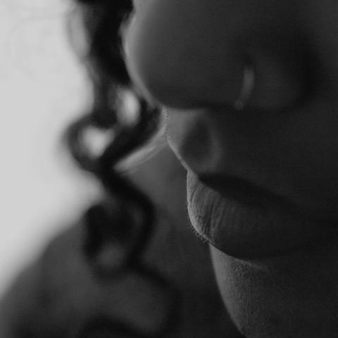 Black-and-white close-up of a person’s lower face and nose in profile, with a blurred chain hanging in the background.