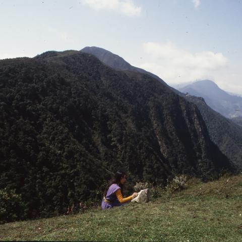 Photo of woman seated writing poetry with tall mountains in the background