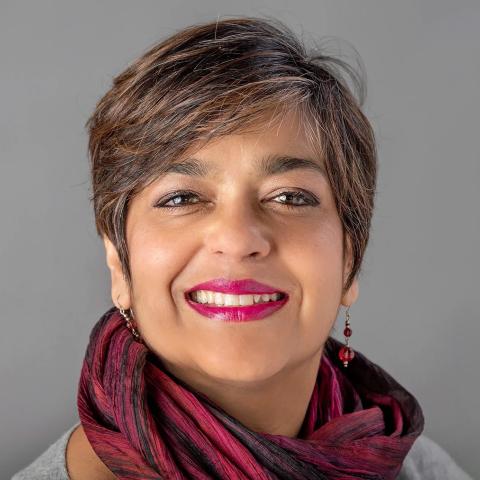 Smiling woman with short dark hair, fuchsia lipstick, and a burgundy scarf, posed against a plain gray background.
