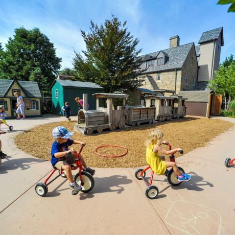 Children riding tricycles on a sidewalk.