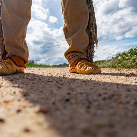 Close up of two feet wearing traditional moccasins standing on pavement 