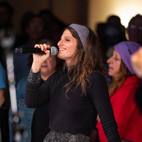 A person singing with workshop attendees in the background.