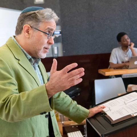 Person behind a lectern speaking into a microphone to a class.