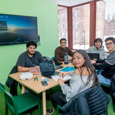 Group of people sitting at a library study table smiling for the camera.