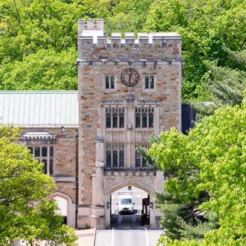 An aerial view of a gothic-style tower gate connected to buildings on either side, with lots of green trees in front and behind it.
