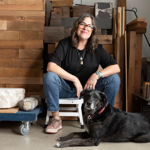 Artist Marie Watt seated in her studio with a dog resting at her feet