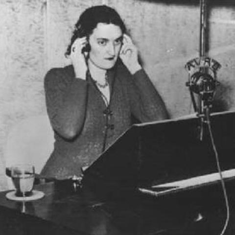 A person sitting at a desk listening intently with her hands pressed to the headphones that cover her ears.