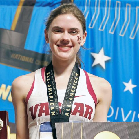 Smiling track athlete holding a trophy at an award ceremony.