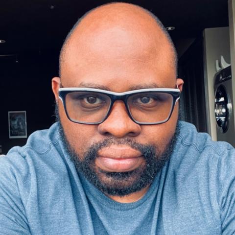 Headshot of a person wearing glasses and a casual shirt, photographed indoors.