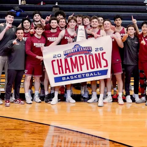 Basketball team on the court, holding a championship banner and posing for a photo.