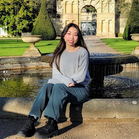 A person with long hair sitting on the edge of an outdoor fountain.