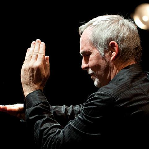 A performer gestures during a live Soundpainting performance on a dark stage, using hand movements to direct real-time improvisation.